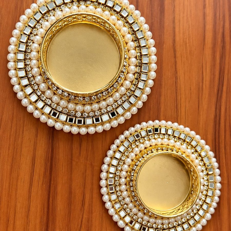 Pair of handmade gold tea light holders with pearl and kundan borders, on a wooden table